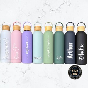 Row of colourful personalised stainless-steel water bottles with engraved names in various fonts, bamboo lids and matte finish, reusable eco drinkware by Etch ’n’ Shine.