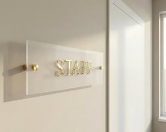 May include: A rectangular frosted acrylic sign mounted to a wall with gold-toned hardware. The sign features the word STAFF in raised, metallic gold lettering centered on the surface. The design includes circular gold standoffs on each side.