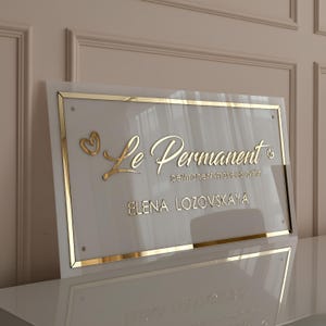 Placa de parede em acrílico com logotipo personalizado em letras douradas. Sinalização de marca para estúdio ou escritório.