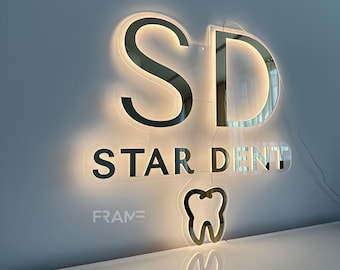 May include: A white illuminated sign with the letters "SD" in gold, the words "STAR DENT" in black, and a white outline of a tooth. The sign has the word "FRAME" in black at the bottom.