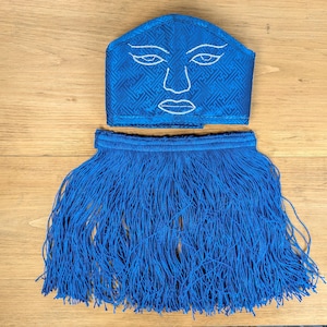 May include: A blue fabric mask with a white embroidered face and a blue fringe trim.
