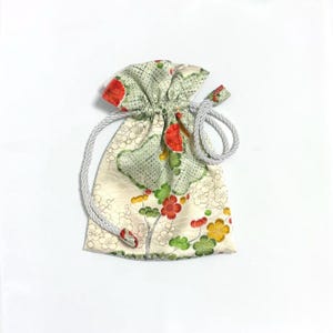 Puede incluir: Una pequeña bolsa con cordón y estampado floral. La bolsa presenta un fondo crema con diseños florales verdes, rojos y amarillos. El cordón es de color gris plateado.