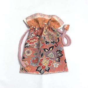 以下が含まれることがあります： コーラル、赤、紫の色合いのフローラルパターンが特徴の小さな巾着袋。 ピンク色の紐と、コントラストのある模様のトリムが付いています。 花柄のデザインには、詳細な葉と花びらが含まれています。