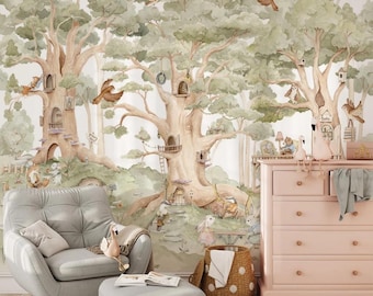 May include: A whimsical nursery scene featuring a large mural of a forest with treehouses and woodland creatures. A gray armchair and ottoman sit in front of the mural, with a pink dresser and a woven basket completing the room's decor.