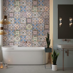 Può includere: Una vasca da bagno bianca con una parete piastrellata dietro. Le piastrelle sono un mix di blu, verde e giallo con motivi intricati. C'è una pianta in un vaso su un supporto accanto alla vasca. Un lavandino con uno specchio e due applique a parete si trova sul lato destro dell'immagine.