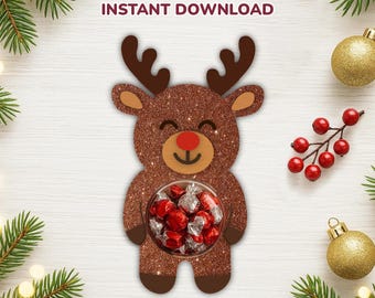 Peut inclure: Un porte-bonbons en forme de renne marron pailleté, avec un nez rouge et un visage souriant, tenant un bol rempli de bonbons emballés. Le texte indique "REINDEER CANDY HOLDER INSTANT DOWNLOAD" et "SVG CUT FILES".