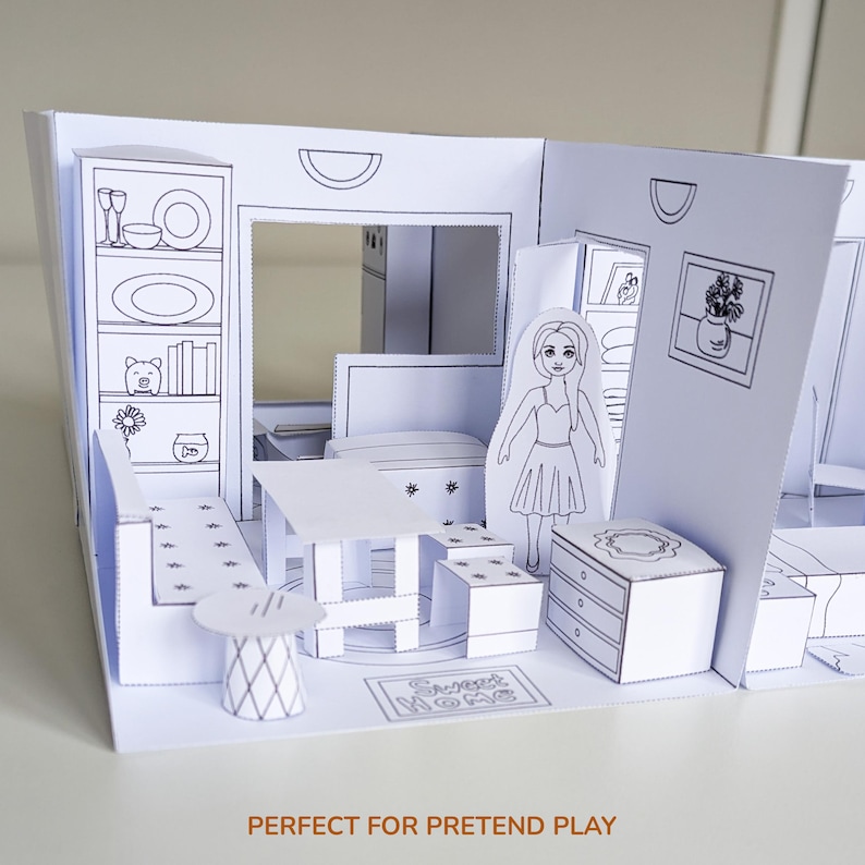 May include: A white paper craft dollhouse with black line art illustrations of furniture, including a dining table, chairs, a dresser, and a bookshelf. A flat paper doll figure stands in the center. The floor features the text Sweet Home.