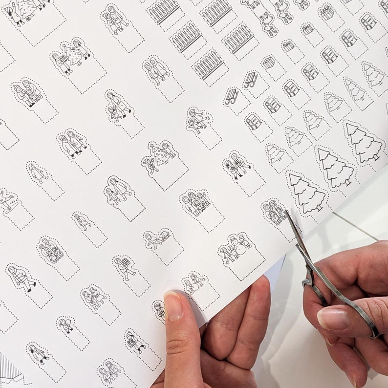 May include: A sheet of white paper with black line art illustrations of Christmas-themed figures and objects. A pair of scissors is cutting out one of the illustrations. The illustrations include Christmas trees, people, and gift boxes.