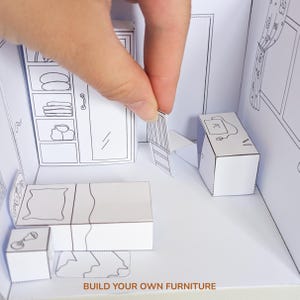 May include: A white paper craft set featuring a miniature bedroom scene with a bed, wardrobe, desk, and chair. The furniture pieces are outlined in black ink, and the text BUILD YOUR OWN FURNITURE is printed at the bottom of the scene.