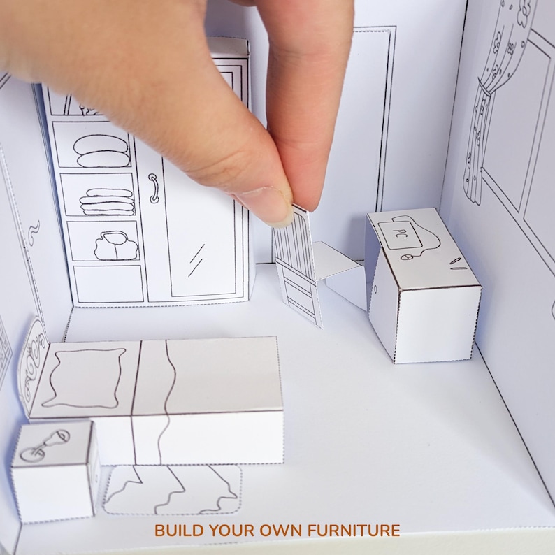 May include: A white paper craft set featuring a miniature bedroom scene with a bed, wardrobe, desk, and chair. The furniture pieces are outlined in black ink, and the text BUILD YOUR OWN FURNITURE is printed at the bottom of the scene.