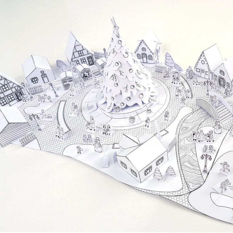 May include: A white paper pop-up Christmas village scene with a central Christmas tree, houses, and figures. The detailed illustration includes a town square, bridge, and various buildings, all in a black and white line drawing style.