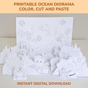 Op de afbeelding: Printbaar oceaan diorama met verschillende zeedieren, waaronder een dolfijn, vissen, een octopus en een zeepaardje. De tekst "PRINTABLE OCEAN DIORAMA COLOR, CUT AND PASTE" en "INSTANT DIGITAL DOWNLOAD" zijn zichtbaar.