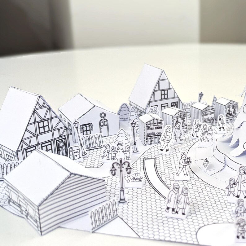 May include: A detailed, black and white papercraft village scene. The pop-up design features buildings, a Christmas tree, and figures of people. The scene includes a street, lampposts, and a snowman, creating a festive holiday atmosphere.