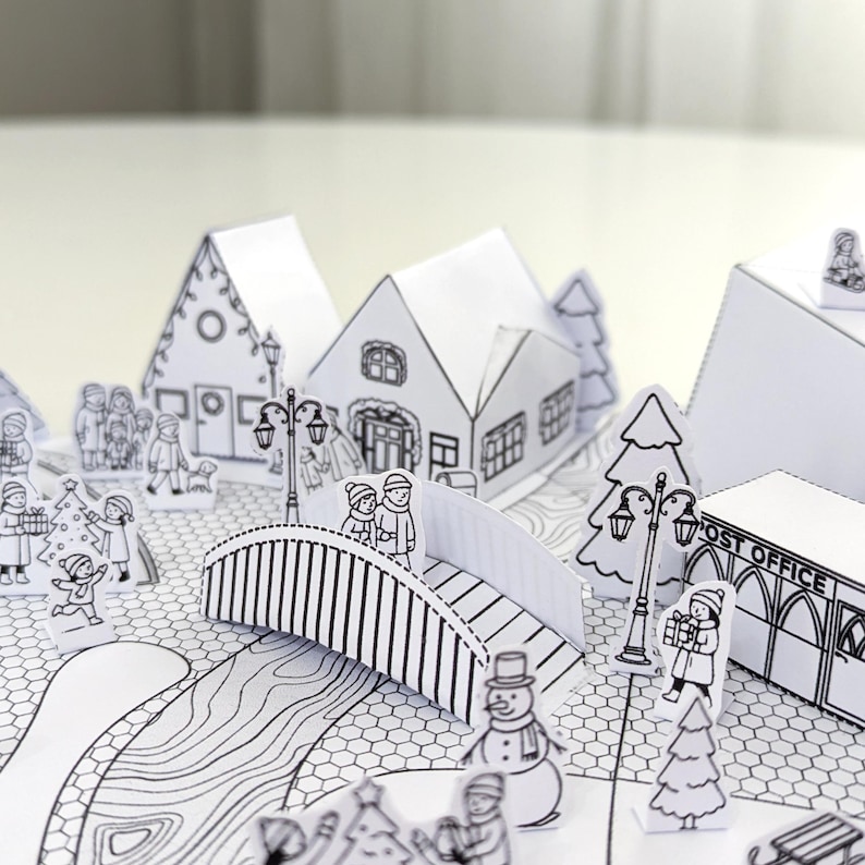 May include: A black and white papercraft winter village scene. The scene includes houses, a bridge, trees, and figures of people. The post office is visible. The overall theme is a winter holiday scene.