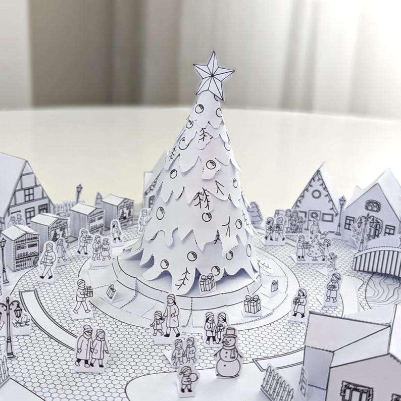 May include: A detailed papercraft Christmas scene featuring a central tree topped with a star. The white tree is surrounded by a town with houses, shops, and people. The scene is entirely in black and white, creating a charming, handcrafted aesthetic.