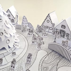 May include: A black and white paper Christmas village scene with a decorated Christmas tree, houses, and figures of people. The scene includes a bridge, street lamps, and gifts. The overall theme is a festive holiday setting.