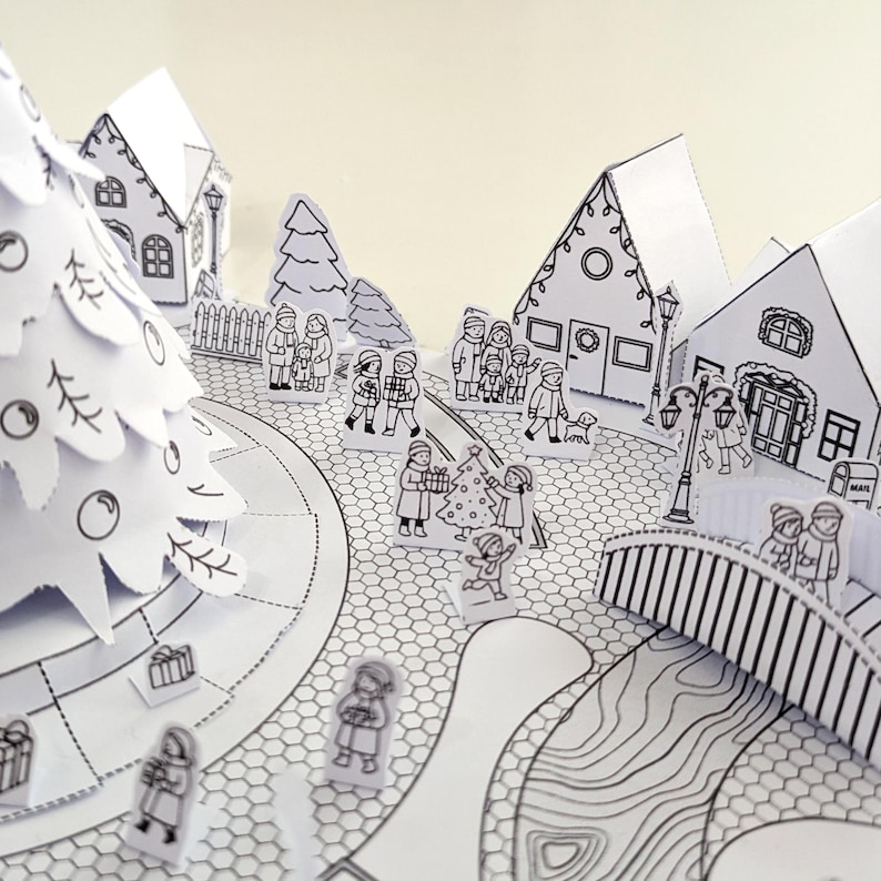 May include: A black and white paper Christmas village scene with a decorated Christmas tree, houses, and figures of people. The scene includes a bridge, street lamps, and gifts. The overall theme is a festive holiday setting.