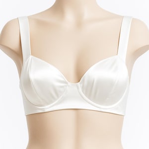 Puede incluir: Sujetador blanco de sat&eacute;n con tirantes anchos. El sujetador tiene un dise&ntilde;o cl&aacute;sico con aros y un acabado liso y sin costuras. El sujetador se muestra en un maniqu&iacute;.
