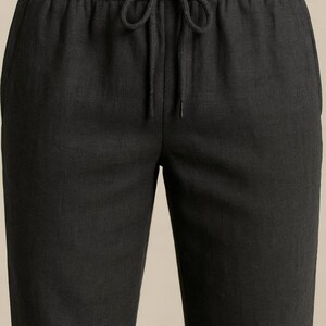 May include: Close-up of dark gray linen pants with an elastic waistband and drawstring. The pants have a relaxed fit and a subtle texture. The drawstring is tied in a bow.