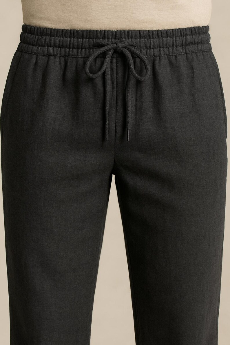 May include: Close-up of dark gray linen pants with an elastic waistband and drawstring. The pants have a relaxed fit and a subtle texture. The drawstring is tied in a bow.