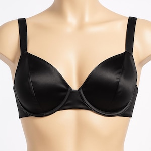 Puede incluir: Un sujetador negro de sat&eacute;n con aros y tirantes ajustables. El sujetador se muestra en un maniqu&iacute;, destacando su textura suave y brillante y su dise&ntilde;o cl&aacute;sico. Las copas son moldeadas.