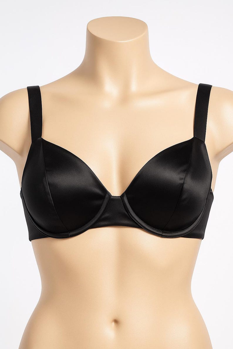 Puede incluir: Un sujetador negro de sat&eacute;n con aros y tirantes ajustables. El sujetador se muestra en un maniqu&iacute;, destacando su textura suave y brillante y su dise&ntilde;o cl&aacute;sico. Las copas son moldeadas.