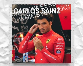 May include: A 2027 wall calendar featuring a photograph of Carlos Sainz wearing a red long-sleeve racing shirt with sponsor logos including Richard Mille, AWS, and Ferrari. The text Carlos Sainz 2027 Calendar is printed at the top.