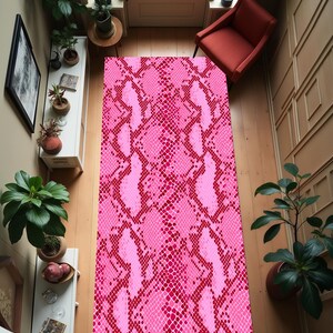 Könnte beinhalten: Ein rechteckiger Teppich mit einem rosa-roten Schlangenhautmuster. Der Teppich befindet sich in einem Raum mit Holzboden, einem roten Stuhl und mehreren Topfpflanzen. Das Muster des Teppichs ist ein sich wiederholendes Schuppenmuster.