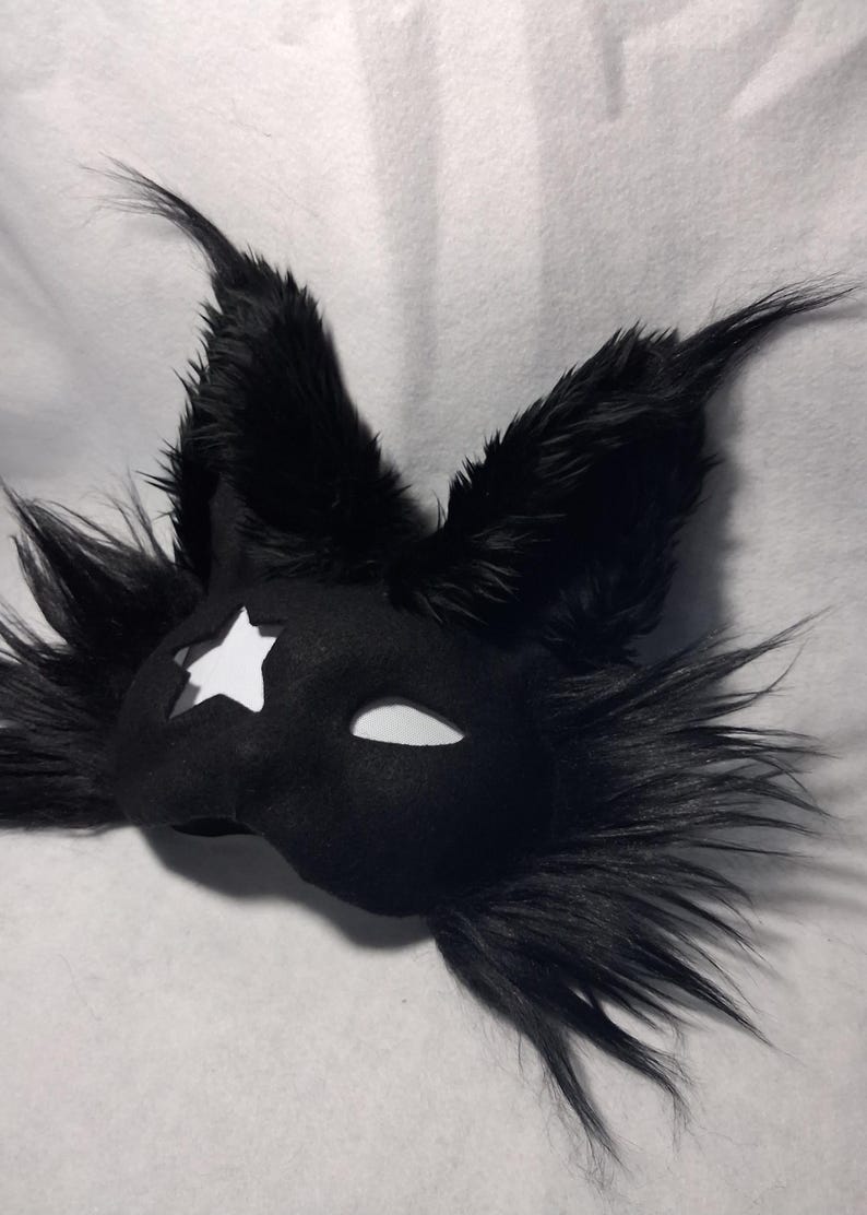 May include: Black felt mask with a star cutout and white eye openings. The mask is adorned with long, black faux fur, giving it a dramatic, animalistic appearance. This costume accessory is suitable for cosplay or themed events.