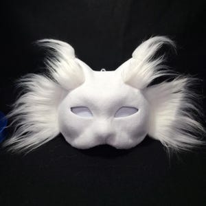 May include: A white felt mask with large, fluffy white fur accents around the ears and cheeks. The mask has eye cutouts and a nose bridge, creating a whimsical, fantasy-inspired design. Ideal for costume parties or cosplay.