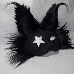 May include: Black mask with a star cutout and fluffy, pointed ears. The mask has a white star on the left side and a white eye cutout on the right. The mask is made of a soft, dark material and is likely for costume or cosplay.