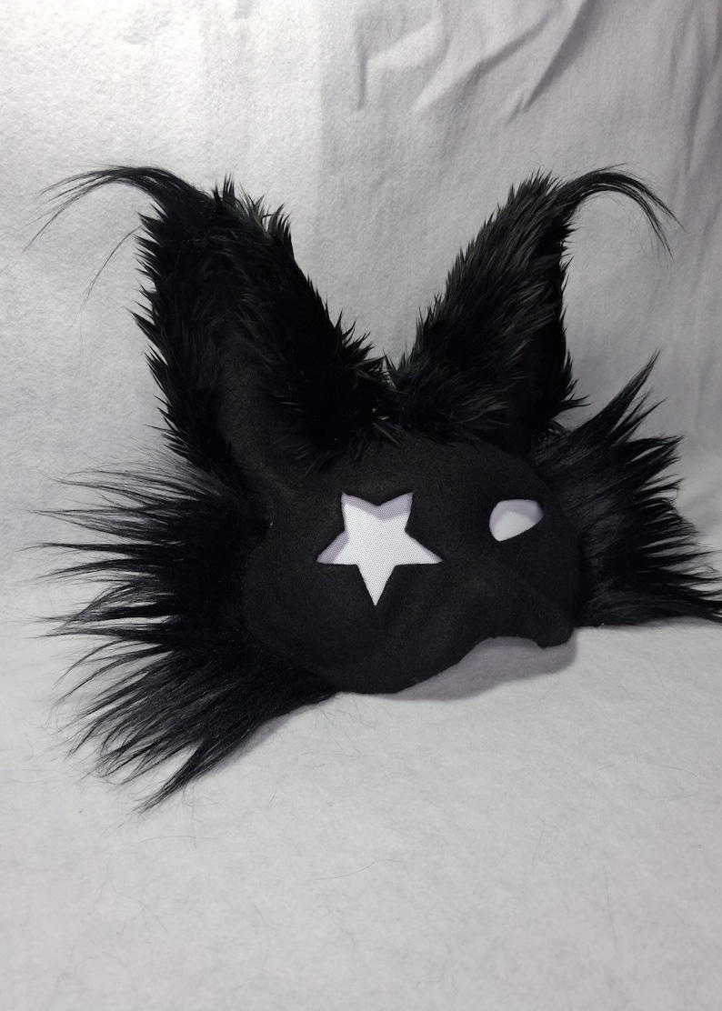 May include: Black mask with a star cutout and fluffy, pointed ears. The mask has a white star on the left side and a white eye cutout on the right. The mask is made of a soft, dark material and is likely for costume or cosplay.