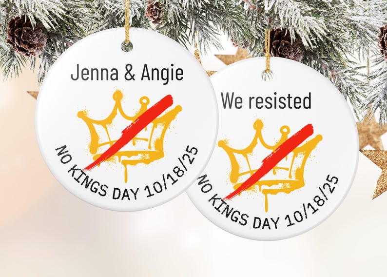 Puede incluir: Dos adornos redondos de cer&aacute;mica blanca con hilo dorado para colgar. Cada adorno presenta un dise&ntilde;o de corona dorada tachado con una raya roja. El texto incluye "Jenna & Angie" y "We resisted", con "No Kings Day 10/18/25".