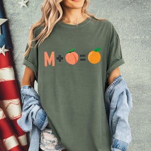 May include: A green t-shirt with a graphic print of a peach, plus sign, and an orange with the text "M + O = ".