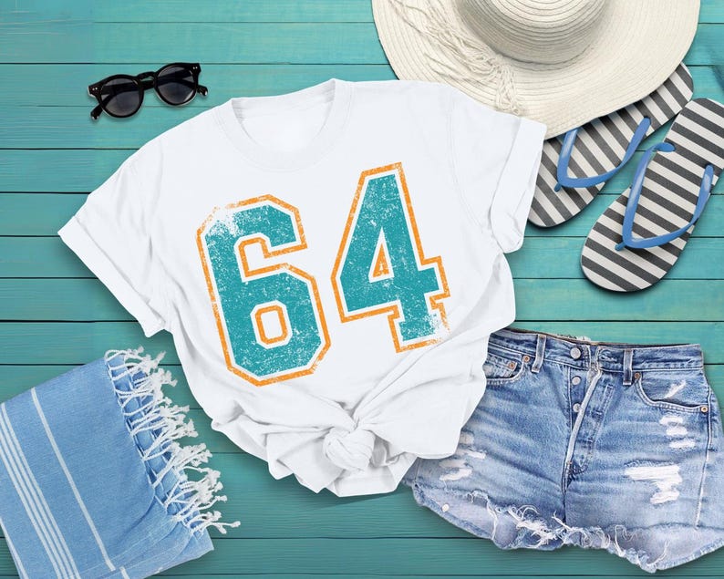 Puede incluir: Camiseta blanca con el n&uacute;mero "64" en turquesa y naranja, con un aspecto desgastado. Se combina con pantalones cortos vaqueros, gafas de sol, un sombrero para el sol y chanclas, evocando el verano.