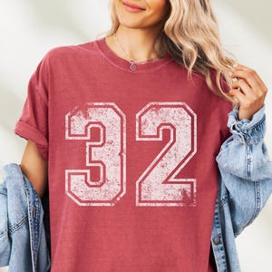 Puede incluir: Camiseta roja con el n&uacute;mero 32 en fuente blanca desgastada. La camiseta tiene mangas cortas y un corte holgado. Se lleva una chaqueta vaquera.