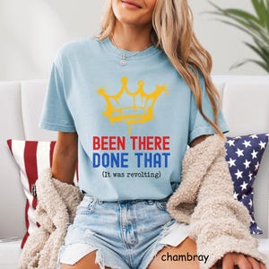 May include: Light blue t-shirt with a yellow crown graphic and the text "BEEN THERE DONE THAT (It was revolting)". The shirt is made of a soft material and is a casual style.
