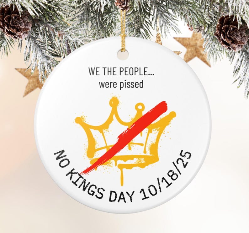 Puede incluir: Adorno navide&ntilde;o redondo de cer&aacute;mica blanca con cord&oacute;n dorado. El adorno presenta el texto "WE THE PEOPLE... were pissed" sobre una corona dorada tachada con una raya roja. Las palabras "NO KINGS DAY 10/18/25" est&aacute;n impresas en la parte inferior.