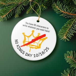 Puede incluir: Un adorno navide&ntilde;o blanco y redondo con una cuerda dorada. El adorno presenta un dise&ntilde;o de corona dorada tachado con una l&iacute;nea roja. El texto incluye "NO KINGS DAY 10/18/25" y "You have 65 characters to write whatever you want here!"