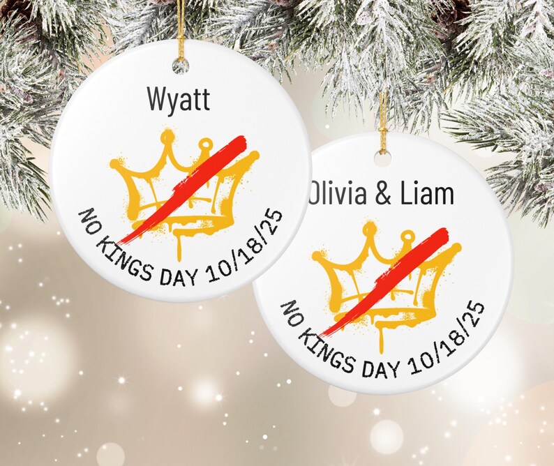 Puede incluir: Dos adornos navide&ntilde;os redondos de cer&aacute;mica blanca con hilo dorado. Cada adorno presenta un dise&ntilde;o de corona dorada tachado con una barra roja, el texto "NO KINGS DAY 10/18/25" y un nombre. Uno dice "Wyatt", el otro "Olivia & Liam".
