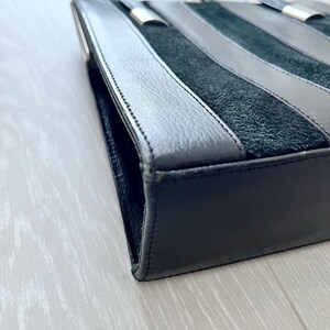 May include: A black leather handbag with a suede panel and silver hardware. The bag has a top handle and a shoulder strap.