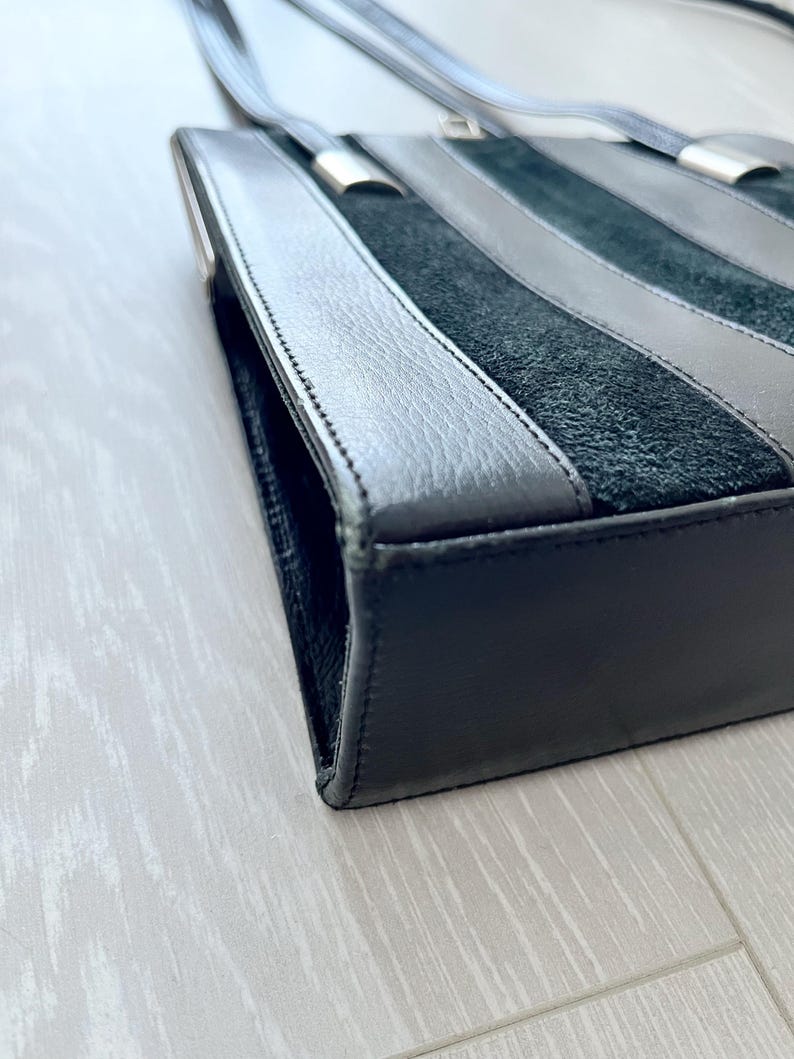 May include: A black leather handbag with a suede panel and silver hardware. The bag has a top handle and a shoulder strap.
