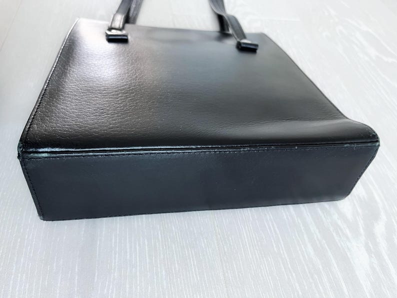 May include: A black leather tote bag with a simple design and two handles.