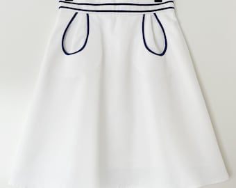 Falda náutica vintage de los años 60, corte en A, ribete de contraste moderno, detalle de bolsillo único, falda blanca hasta la rodilla de mediados de siglo.