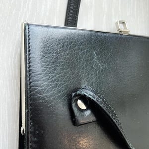 May include: A black leather clutch bag with a silver clasp and a silver handle. The bag has a textured leather surface.