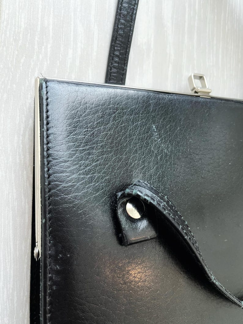 May include: A black leather clutch bag with a silver clasp and a silver handle. The bag has a textured leather surface.