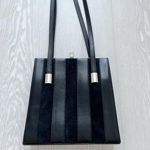 May include: A black leather handbag with vertical stripes and silver hardware. The bag has a top handle and a shoulder strap.