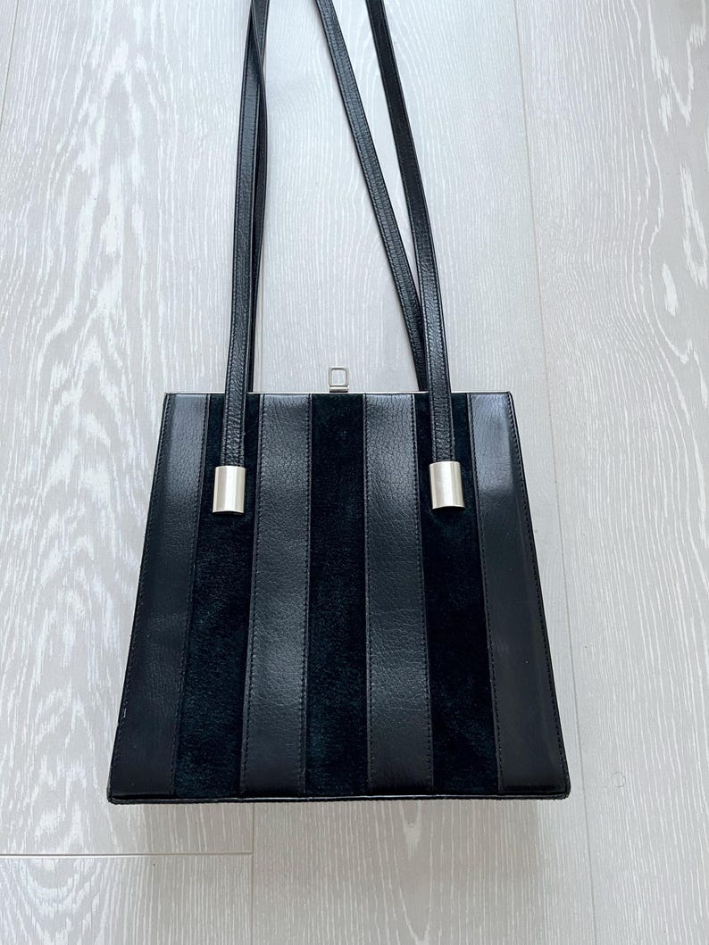 May include: A black leather handbag with vertical stripes and silver hardware. The bag has a top handle and a shoulder strap.