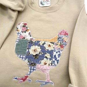 Quilt like printed fabric appliqued on a sand colored Gildan sweatshirt. Sweatshirt has sleeves rolled and is on the applique fabric. Fabric used is "B" cottagecore patchwork fabric.