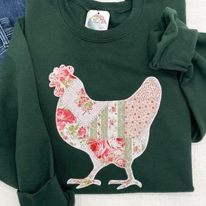 Embroidered chicken on a green sweatshirt. Fabric is a printed patchwork design with shades of pink florals and sage.